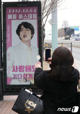 본문 이미지 - 12일 서울 용산구 하이브 사옥 앞 버스정류장에서 일본인 팬이 군입대를 앞둔 그룹 방탄소년단(BTS)의 멤버 진을 응원하는 광고현수막 사진을 찍고 있다. 2022.12.12/뉴스1 ⓒ News1 박세연 기자
