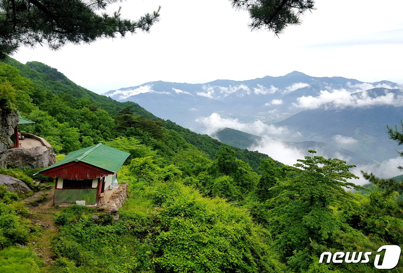본문 이미지 - 문수암 풍경. 사진의 녹색지붕 절집은 무너져 철거되었고, 왼쪽 끝 바위 밑의 법당만 남아있다. 지리산 건너 삼봉산이 아득하다 ⓒ 뉴스1