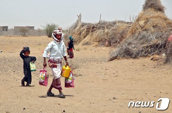 수 백만명이 기아 위기에 처해있는 홍해 연안 예멘 호데이다 서부 헤이스 지역 난민 캠프에서 구호 식량과 물품을 들고 한 남성과 아이가 걸어가고 있다. 2022.03.29 © AFP=뉴스1 © News1 정윤미 기자