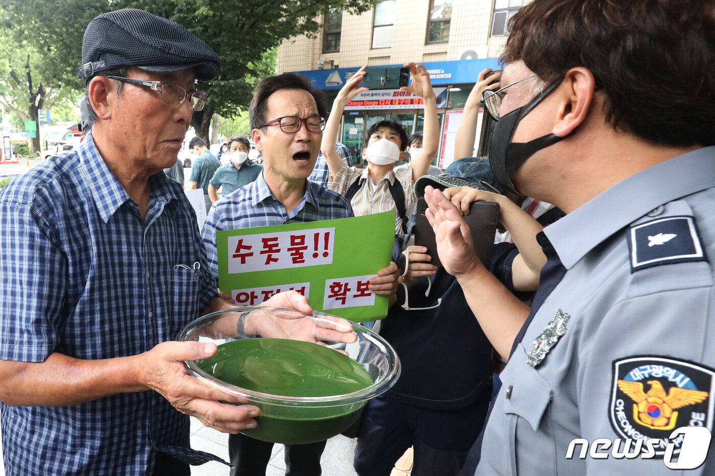 본문 이미지 - 낙동강네트워크·낙동강대구경북네트워크 등 영남권 환경단체 회원들이 대구시청 동인청사 앞에서 대구 수돗물 녹조 독소 오염 파동에 대해 항의하며 달성군 매곡정수장 인근 낙동강에서 퍼온 물을 투명 용기에 따른 뒤 청사 정문 앞에서 청원경찰과 대치하고 있다. 2022.8.1 ⓒ 뉴스1 공정식 기자