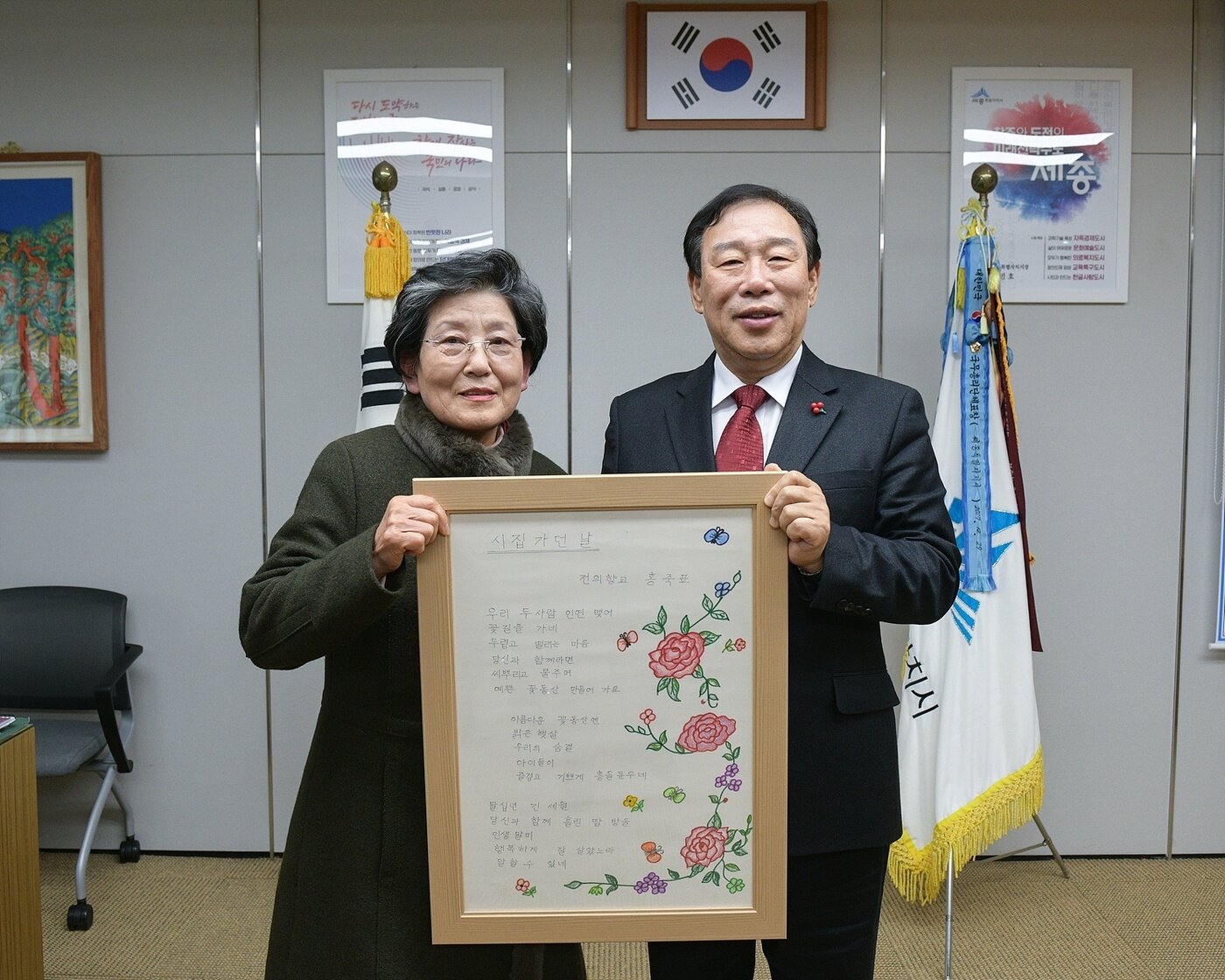 본문 이미지 - 최민호 세종시장이 17일 자신의 집무실에서 세종글꽃체 주인공인 홍죽표 할머니(왼쪽)와 만나 기념촬영을 하고 있다. 들고 있는 것은 2021년 교육부와 국가평생교육진흥원이 주관한 ‘성인 문해교육 시화전’에서 우수상을 받은 홍 할머니의 '시집가던 날' 시화 표구. (세종시 제공) / 뉴스1