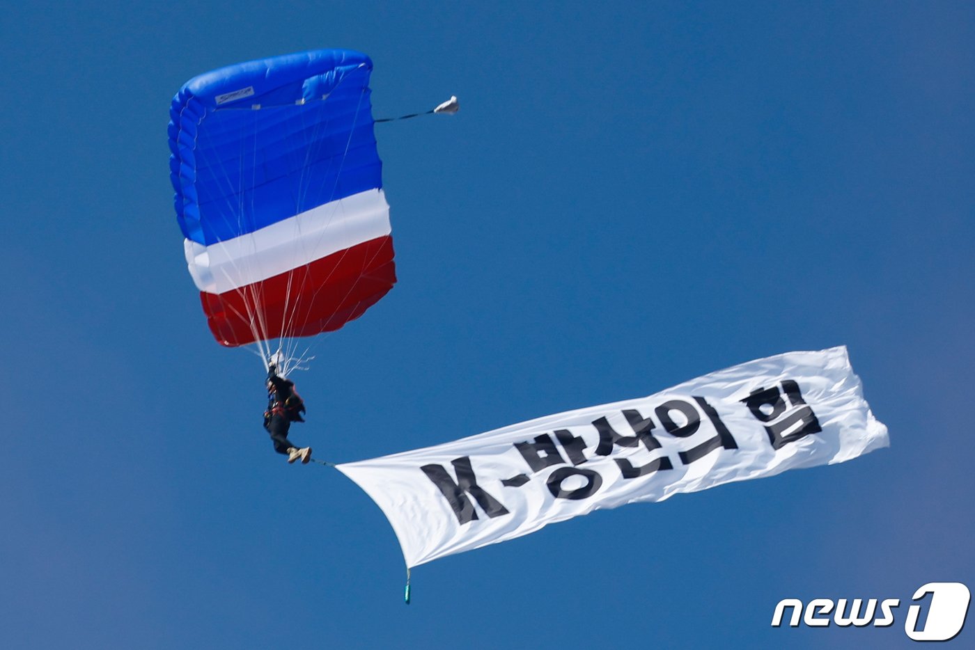 본문 이미지 - 16일 경기 성남시 서울공항에서 열린 서울 국제 항공우주·방위산업 전시회(ADEX) 2023 프레스 데이 행사 중 우리 공군 장병이 낙하산을 매고 'K방산의 힘' 현수막을 펼친 채 하강하고 있다. 2023.10.16/뉴스1 ⓒ News1 안은나 기자