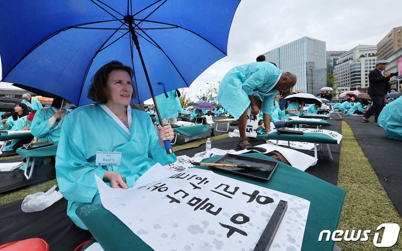 본문 이미지 - 577돌 한글날인 9일 오전 서울 광화문광장에서 열린 휘호경진대회에서 참가자들이 우산으로 비를 막으며 정성스럽게 글씨를 써내려가고 있다. 2023.10.9/뉴스1 ⓒ News1 이동해 기자
