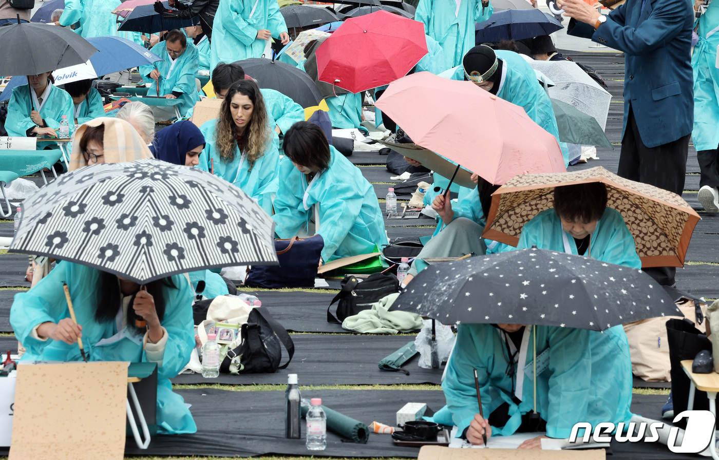 (서울=뉴스1) 이동해 기자 = 577돌 한글날인 9일 오전 서울 광화문광장에서 열린 휘호경진대회에서 참가자들이 우산으로 비를 막으며 정성스럽게 글씨를 써내려가고 있다. 2023. …