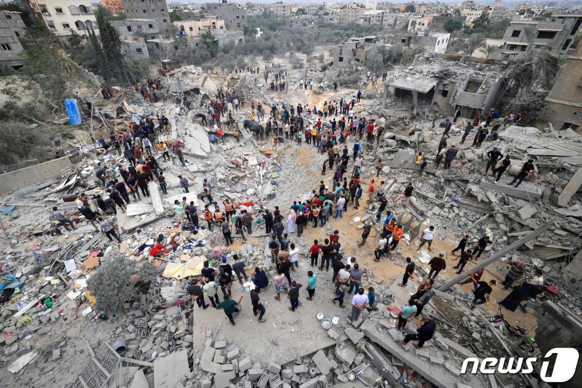 12일(현지시간) 이스라엘의 공격으로 무너진 가자지구 칸 유니스 지역의 건물 사이로 구조대원들과 주민들이 서있다. 2023.11.13 © AFP=뉴스1 © News1 정지윤 기
