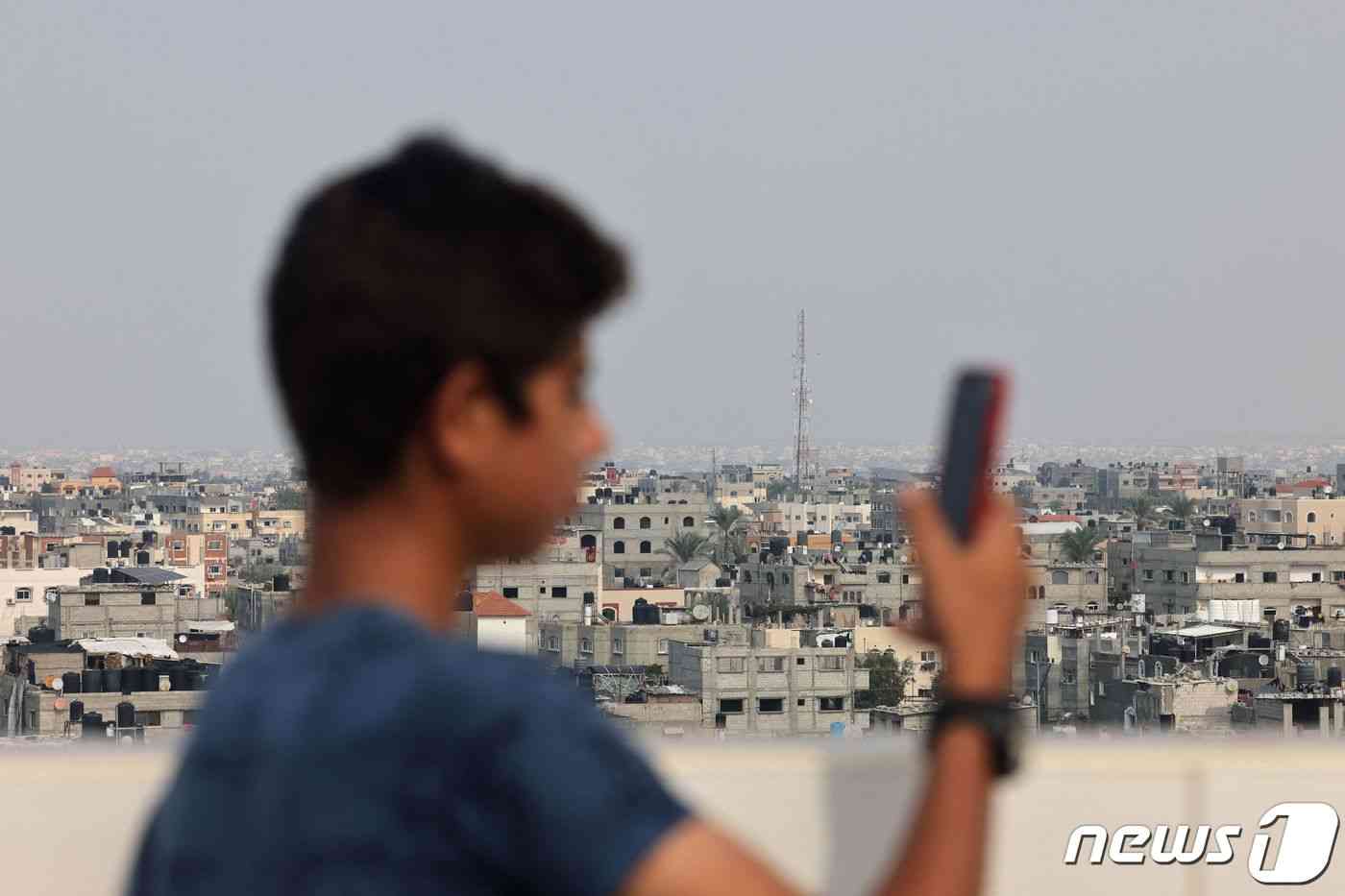 지난달 28일(현지시간) 가자지구 남부 라파에서 현지 주민이 휴대전화를 사용하고 있는 가운데 주민 뒤로 통신탑이 보인다. 2023.10.28. © AFP=뉴스1 © News1 김성식 기자