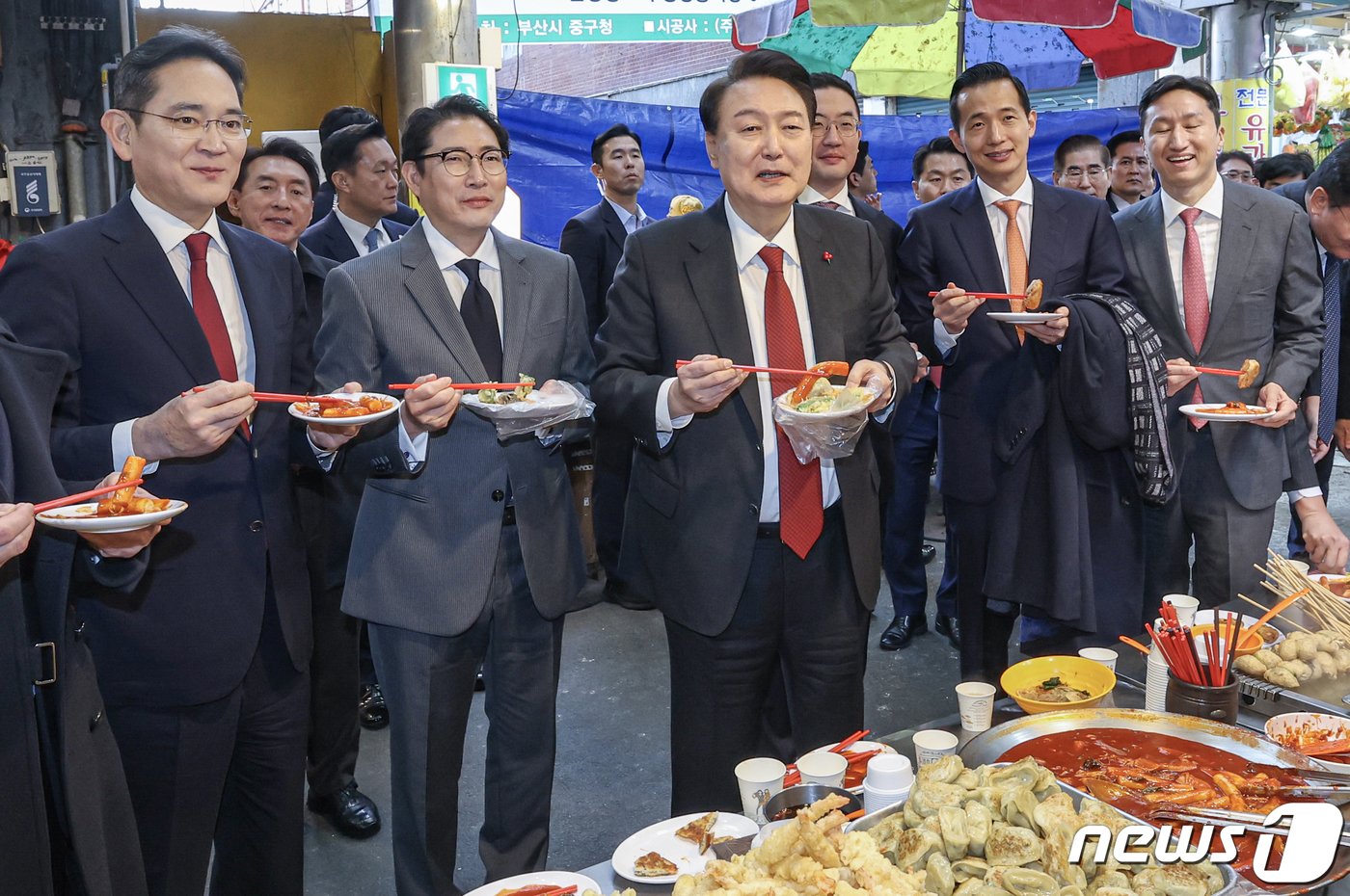 윤석열 대통령이 6일 부산 중구 깡통시장을 방문해 박형준 부산시장과 이재용 삼성전자 회장, 구광모 LG그룹 회장, 조현준 효성그룹 회장, 김동관 한화그룹 부회장, 최재원 SK수석부회장 등 기업총수들과 함께 떡볶이, 튀김, 빈대떡을 맛보고 있다. 2023.12.6/뉴스1 ⓒ News1 부산사진공동취재단