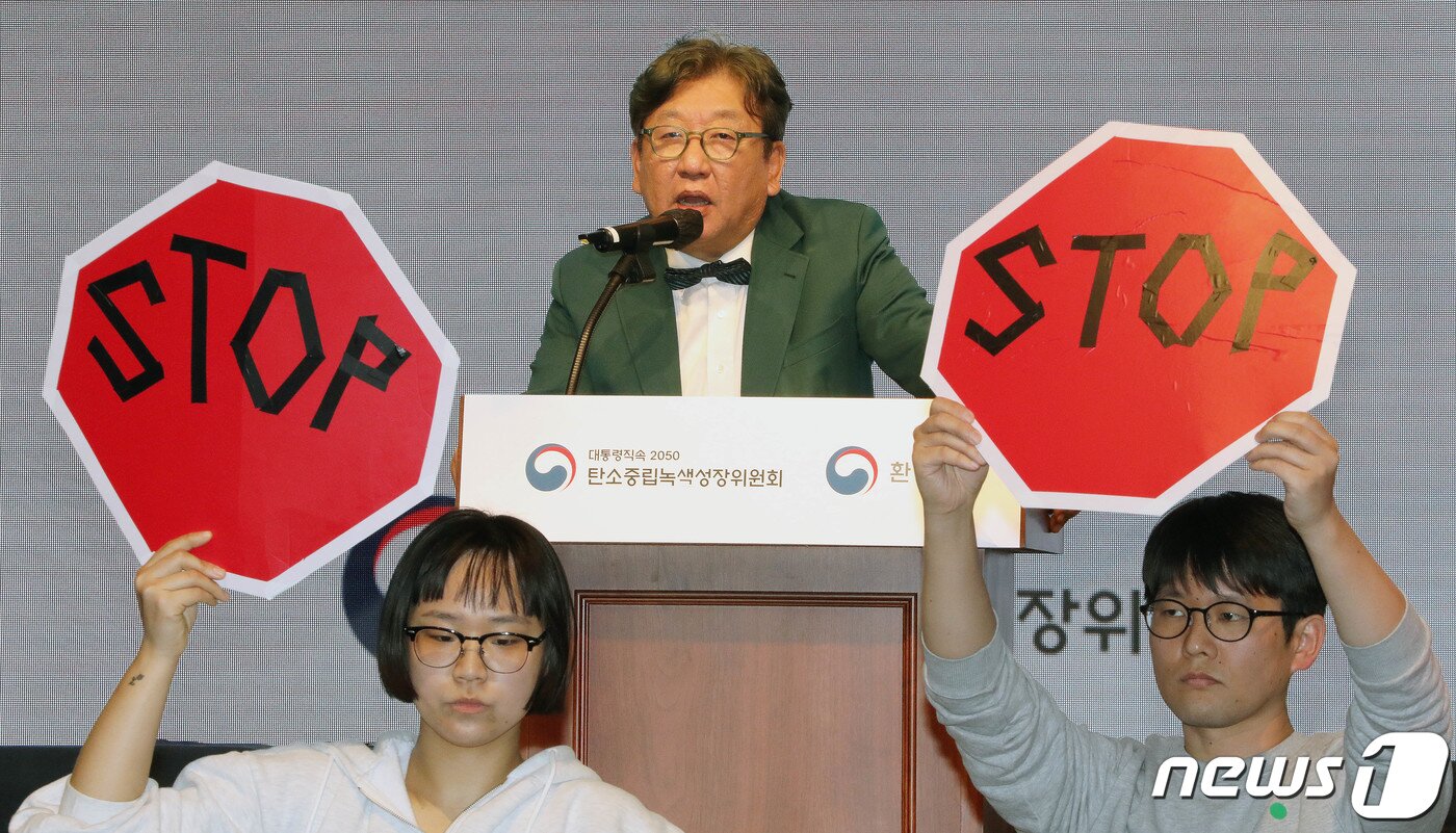 본문 이미지 - 김상협 탄소중립녹색성장위원장이 22일 서울 강남구 한국과학기술회관에서 열린 국가탄소중립 녹색성장 기본계획 수립 등에 대한 공청회에서 발언하고 있는 가운데 환경단체 회원들이 기본계획 철회를 촉구하며 피켓 시위를 하고 있다. 2023.3.22/뉴스1 ⓒ News1 박세연 기자