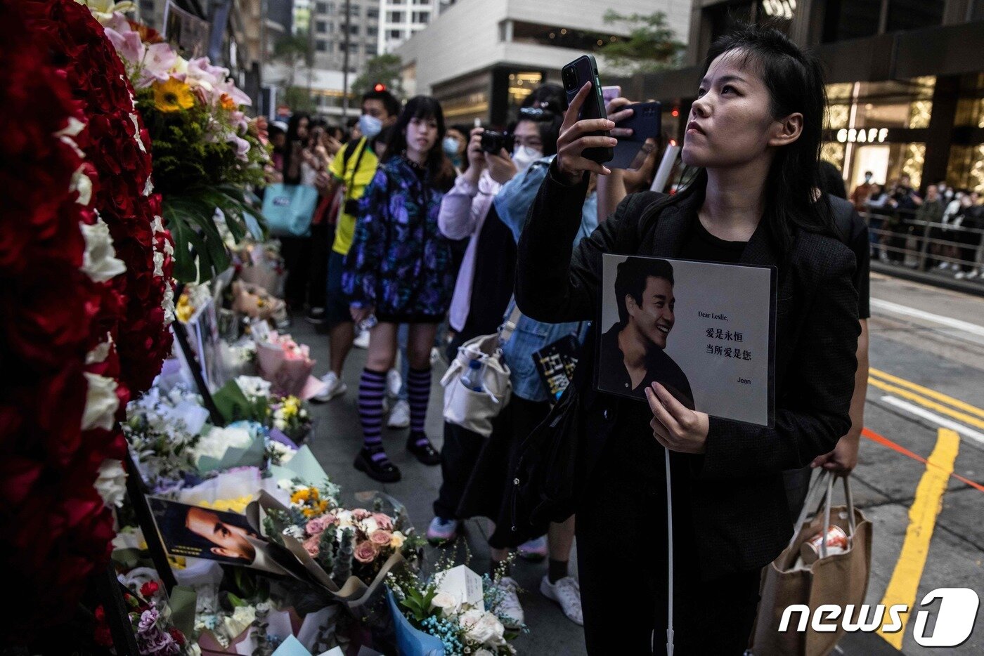 본문 이미지 - 홍콩의 가수 겸 배우였던 장국영의 사망 20주기를 맞은 1일(현지시간) 홍콩에서 시민들이 길가에 놓인 추모 화환과 그의 생전 모습을 카메라에 담고 있다. 2023.04.01. ⓒ AFP=뉴스1 ⓒ News1 김성식 기자