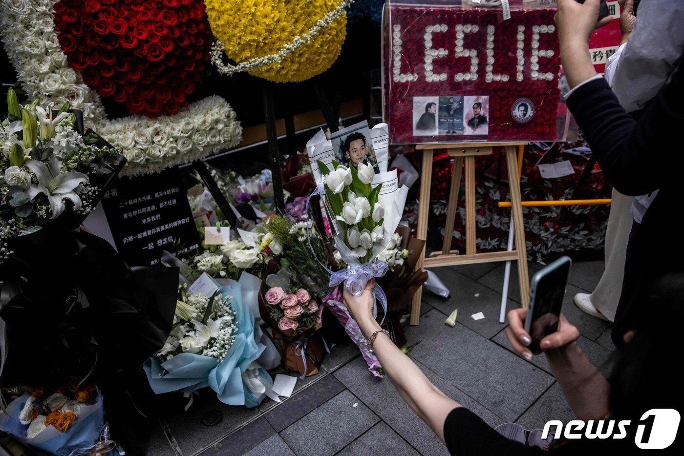 본문 이미지 - 홍콩의 가수 겸 배우였던 장국영의 사망 20주기를 맞은 1일(현지시간) 홍콩에서 시민들이 길가에 놓인 추모 화환과 그의 생전 모습을 카메라에 담고 있다. 2023.04.01. ⓒ AFP=뉴스1 ⓒ News1 김성식 기자