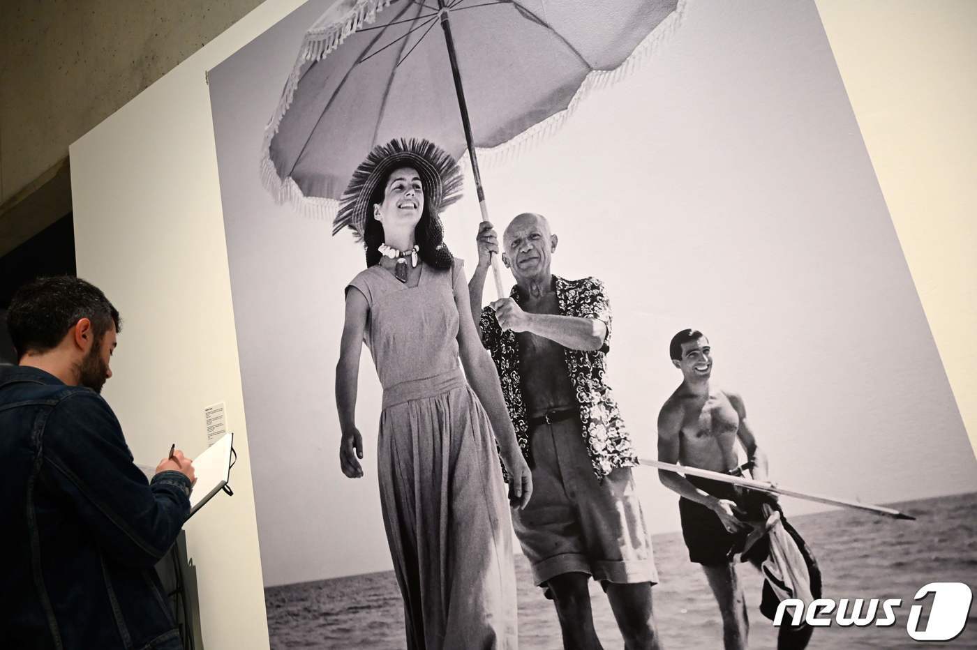 본문 이미지 - 1948년 8월 프랑스 앙티브와 칸 사이 골프-주앙의 해변에서 헝가리 출신 로버트 카파가 사진 촬영한 피카소와 그의 연인 프랑수아즈 질로, 그의 조카 하비르 빌라토의 모습. 2019년 6월5일 한 남성 기자가 스페인 바르셀로나 피카소박물관에 전시된 이 사진 앞에서 메모를 하고 있다. ⓒ AFP=뉴스1 ⓒ News1 정윤미 기자