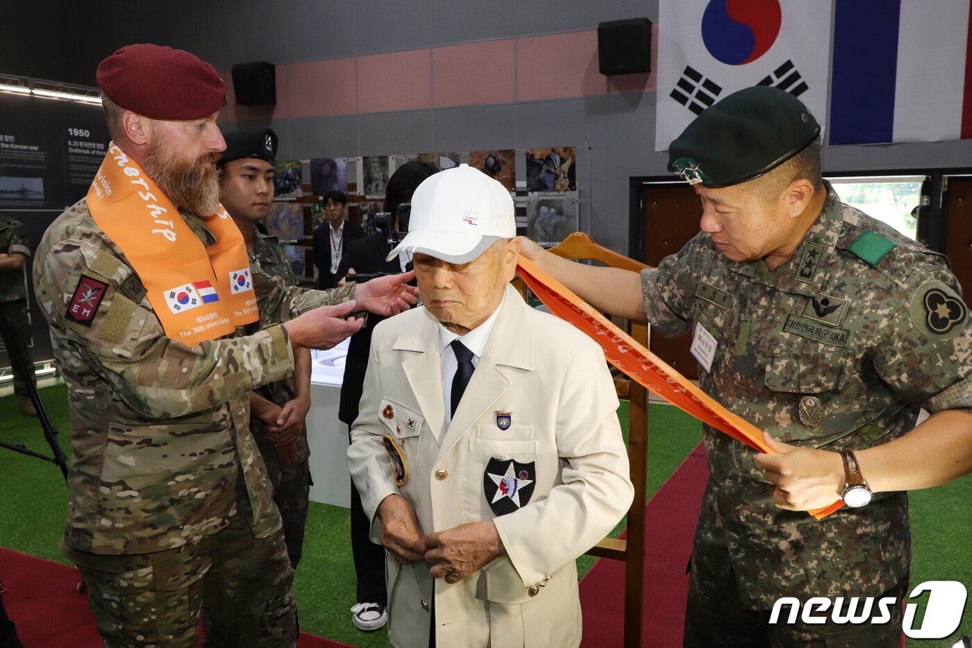 본문 이미지 - 12일 강원도 원주 육군36사단에서 반호이츠 부대원과 함께 6·25전쟁에 참전했던 최병수 옹(가운데)에게 하헌철 사단장(오른쪽)과 반호이츠부대장이 존경과 감사의 마음을 담아 새 제복을 입혀드리고 있다. (육군 제공) 2023.7.12/뉴스1