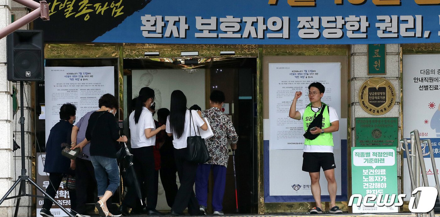 본문 이미지 - 총파업에 돌입한 민주노총 산하 보건의료노조원이 13일 서울 동대문구 경희대병원 입구에서 처우개선, 공공의료 확충 등을 요구하는 구호를 외치는 가운데 환자 및 보호자들이 병원으로 들어서고 있다. 2023.7.13/뉴스1 ⓒ News1 박지혜 기자