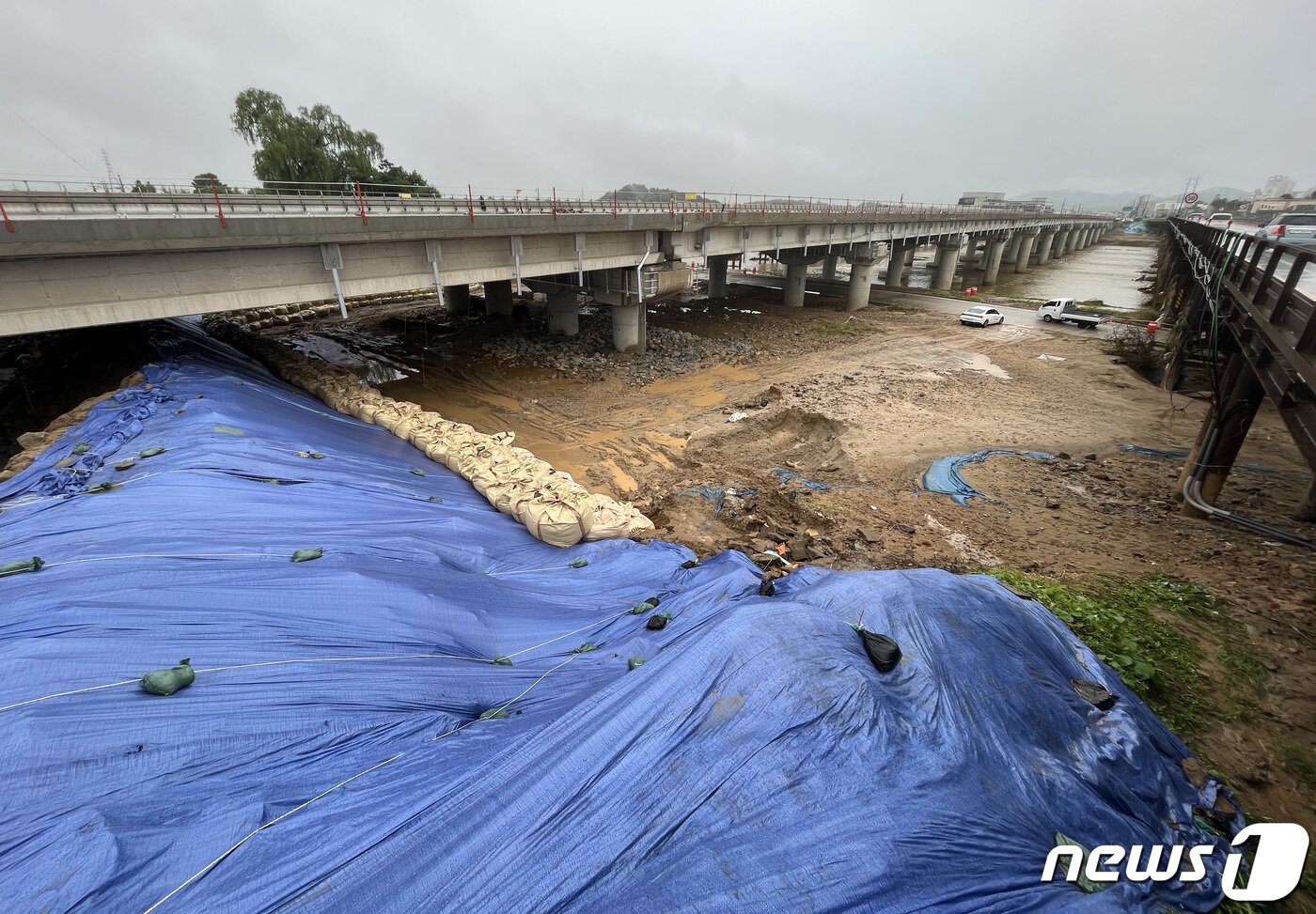 본문 이미지 - 14명의 사망자가 발생한 오송 지하차도 참사의 시작이 된 미호천교 재가설 공사 현장. 참사 사흘이 지난 18일 충북 청주시 오송읍 궁평지하차도 인근 미호강 임시 제방에 방수포와 함께 모래주머니가 둘러져 있다. 2023.7.18/뉴스1 ⓒ News1 구윤성 기자