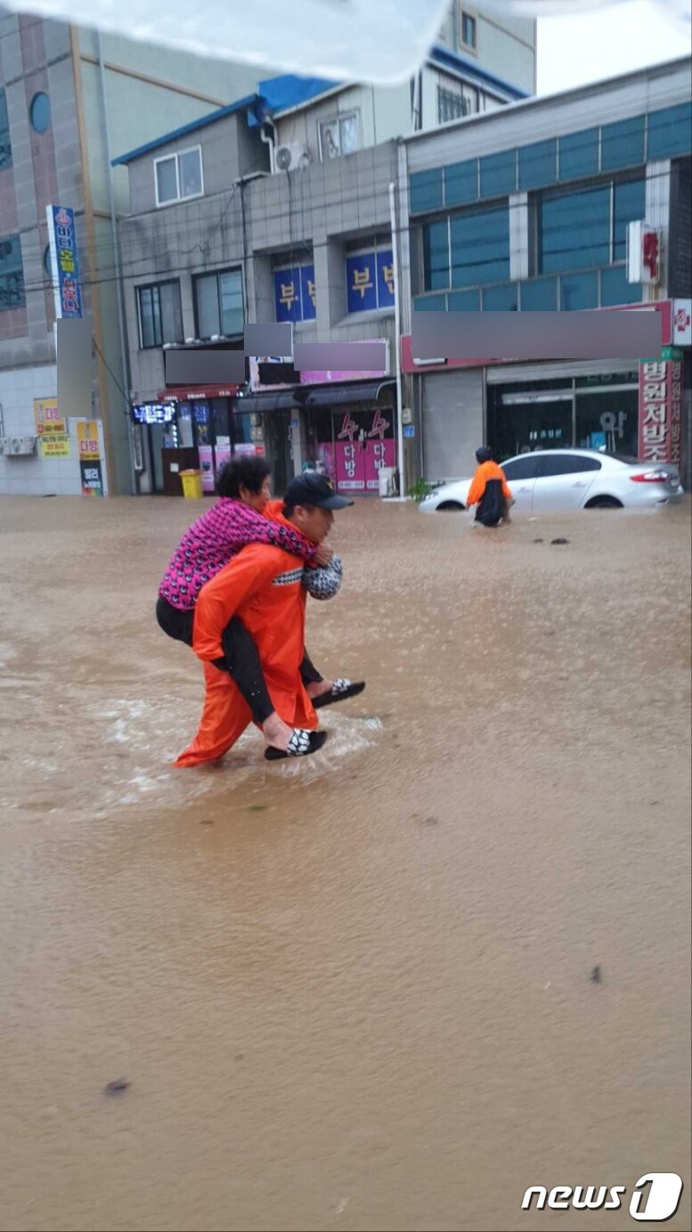 본문 이미지 - 제6호 태풍 '카눈'이 북상한 10일 오후 강원 고성군 거진읍에서 불어난 물에 도로가 침수, 소방대원이 고립된 어르신을 업어 구조하고 있다. (소방청 제공) 2023.8.10/뉴스1