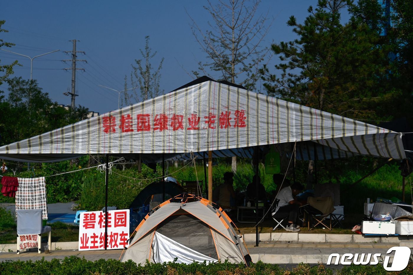 본문 이미지 - 15일 베이징의 최근 디폴트 위기를 맞고 있는 컨트리 가든 공사 현장 옆에서 주민들이 항의 농성을 벌이고 있다. ⓒ AFP=뉴스1 