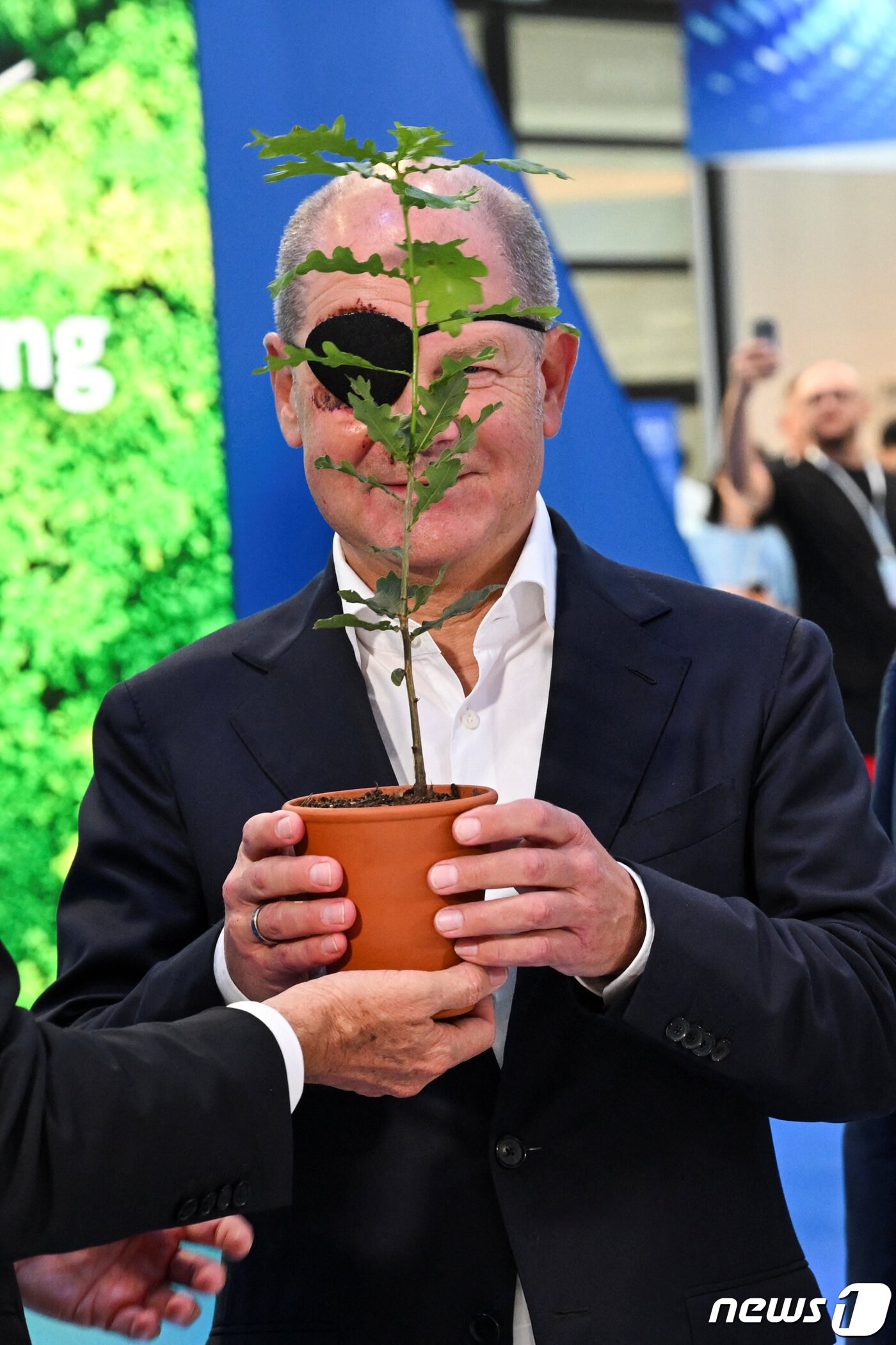 본문 이미지 - 숄츠 총리가 안대를 가리려는 듯 화분을 들어 보이고 있다. ⓒ 로이터=뉴스1 ⓒ News1 우동명 기자