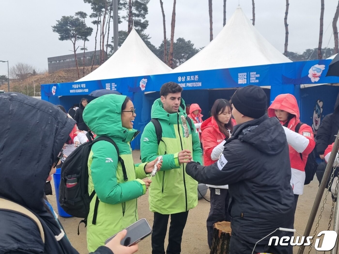 본문 이미지 - 2024 강원 동계청소년올림픽 개막일인 19일 개막식이 열리는 강릉올림픽 파크에 마련된 한국음식 체험부스에서 외국인방문객이 화덕에 구워진 가래떡을 받아들고 있다. 2024.1.19/뉴스1 윤왕근 기자