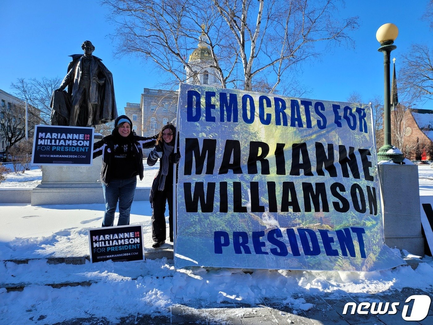 본문 이미지 - 미국 뉴햄프셔주 프라이머리를 이틀 앞둔 21일(현지시간) 주도인 콩코드에 있는 주청사 앞에서 민주당 대선후보 경선에 출마한 작가 매리언 윌리엄슨 후보 지지자인 엘리자베스 트루먼이 딸과 함께 지지 활동을 하고 있다. 2024.01.21.