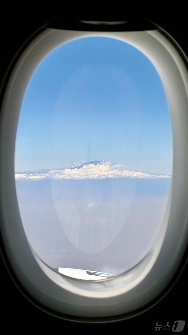 본문 이미지 - 킬리만자로 국제공항으로 가는 환승 비행기 안에서 유리창을 통해 본 킬리만자로 봉우리. 흰 구름 위로 솟은 봉우리가 바다에 떠있는 섬같다.2024.10.4./뉴스1 ⓒ News1 조영석 기자