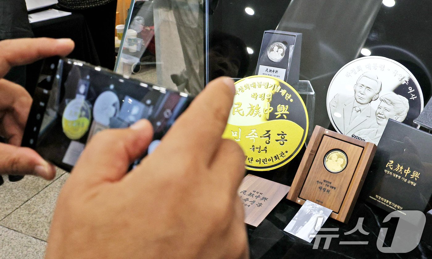 본문 이미지 - 20일 오후 서울 마포구 마포아트센터에서 열린 박정희 전 대통령과 육영수 여사의 첫 공식 기념메달 공개 행사를 찾은 시민이 메달을 촬영하고 있다. 2024.11.20/뉴스1 ⓒ News1 장수영 기자