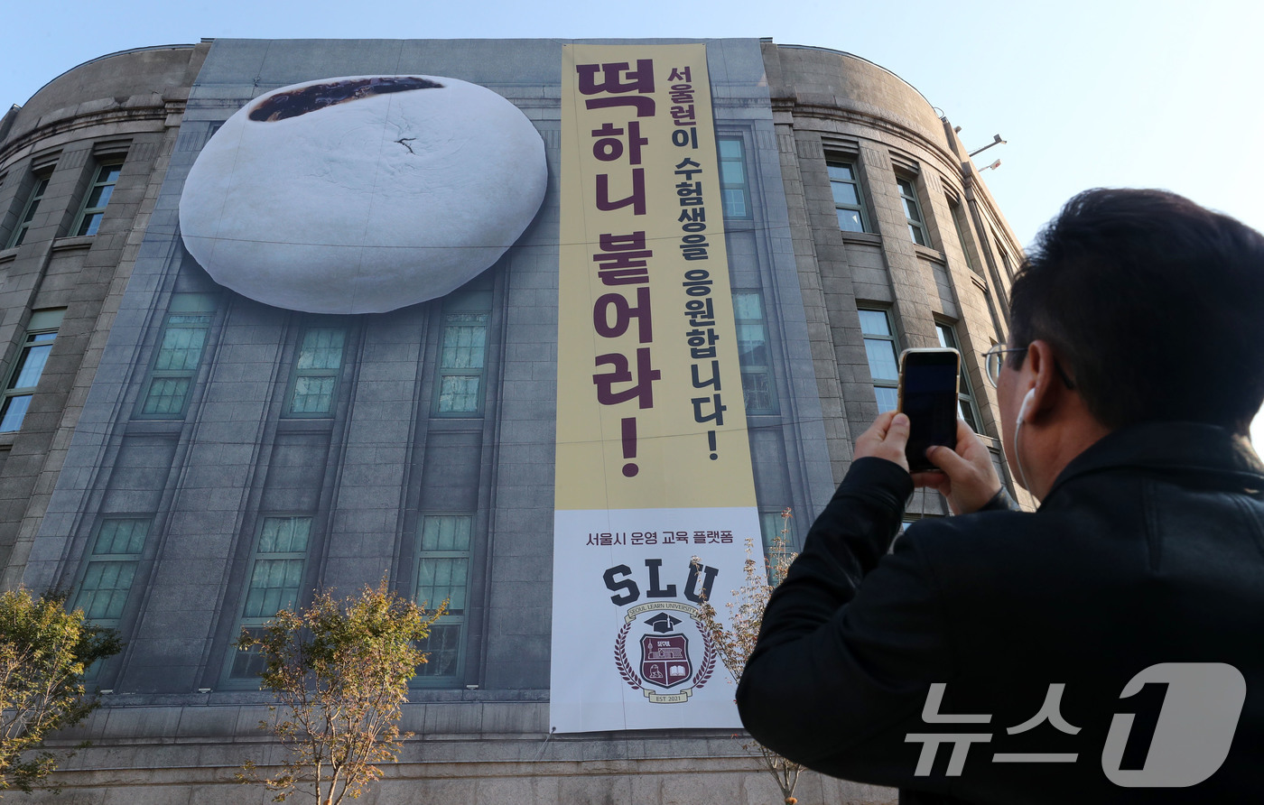 (서울=뉴스1) 박세연 기자 = 2025학년도 대학수학능력시험을 6일 앞둔 8일 오전 한 시민이 서울 중구 서울도서관 외벽에 걸린 수험생을 응원하는 대형 현수막 사진을 찍고 있다. …