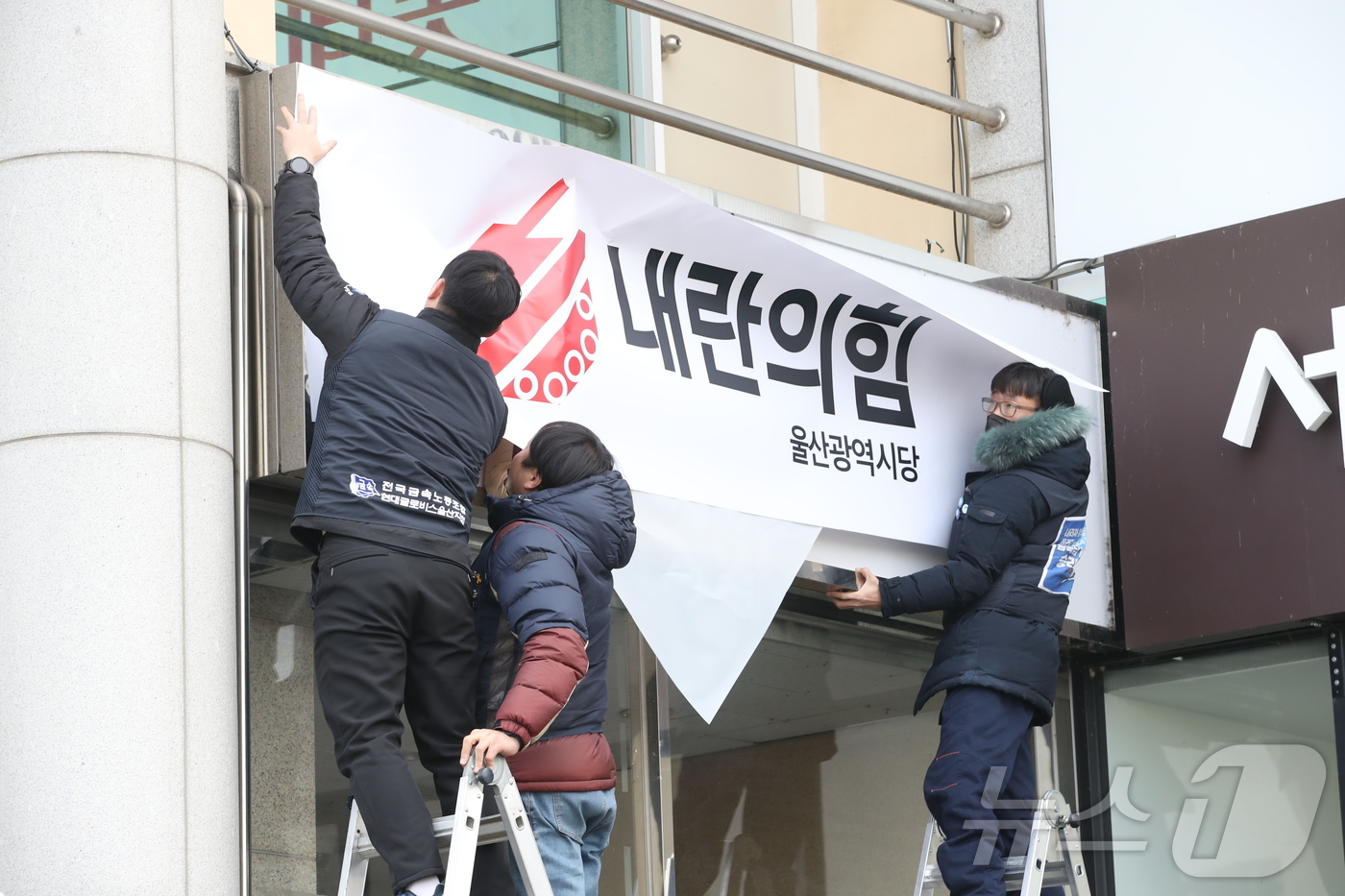 (울산=뉴스1) 김세은 기자 = 윤석열퇴진울산운동본부 관계자들이 11일 오전 국민의힘 울산시당 현판을 '내란의힘'으로 덮고 있다. 2024.12.11/뉴스1