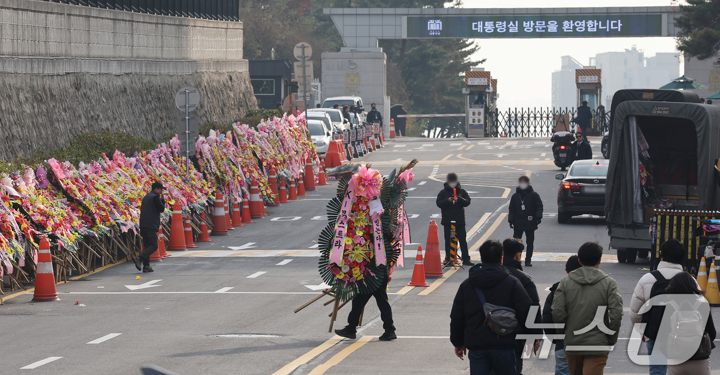 (서울=뉴스1) 장수영 기자 = 11일 오후 서울 용산구 대통령실 출입문 앞 도로에서 화환 업체 관계자가 윤석열 대통령 지지자들이 보낸 화환을 옮기고 있다. 2024.12.11/뉴 …