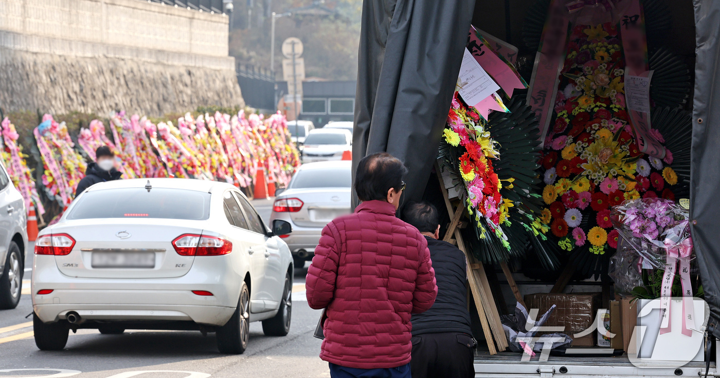 (서울=뉴스1) 장수영 기자 = 11일 오후 서울 용산구 대통령실 출입문 앞 도로에서 화환 업체 관계자가 윤석열 대통령 지지자들이 보낸 화환을 옮기고 있다. 2024.12.11/뉴 …