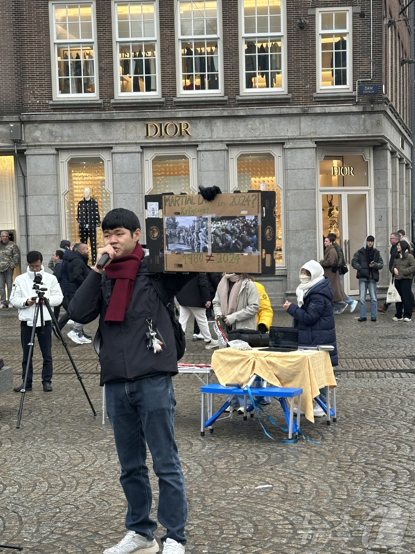 본문 이미지 - 14일&#40;현지시간&#41; 네덜란드 암스테르담 담 스퀘어에서 광주 출신의 한 유학생이 광주의 참상을 알리는 사진과 현재를 비교하며 윤석열 대통령의 퇴진을 요구하고 있다. 2024.12.14/ⓒ 뉴스1 차현정 통신원