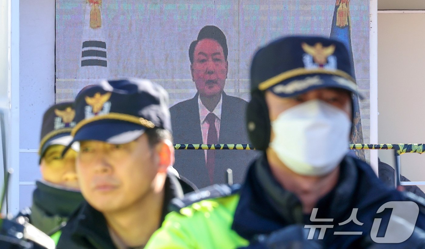 공수처와 경찰 등으로 꾸려진 공조수사본부가 윤석열 대통령에게 통보한 2차 소환일을 하루 앞둔 24일 서울 용산구 대통령 관저 앞에서 경계 근무하는 경찰 뒤로 보수단체가 준비한 윤석열 대통령의 대국민 담화 영상이 나오고 있다. 2024.12.24/뉴스1 ⓒ News1 김성진 기자