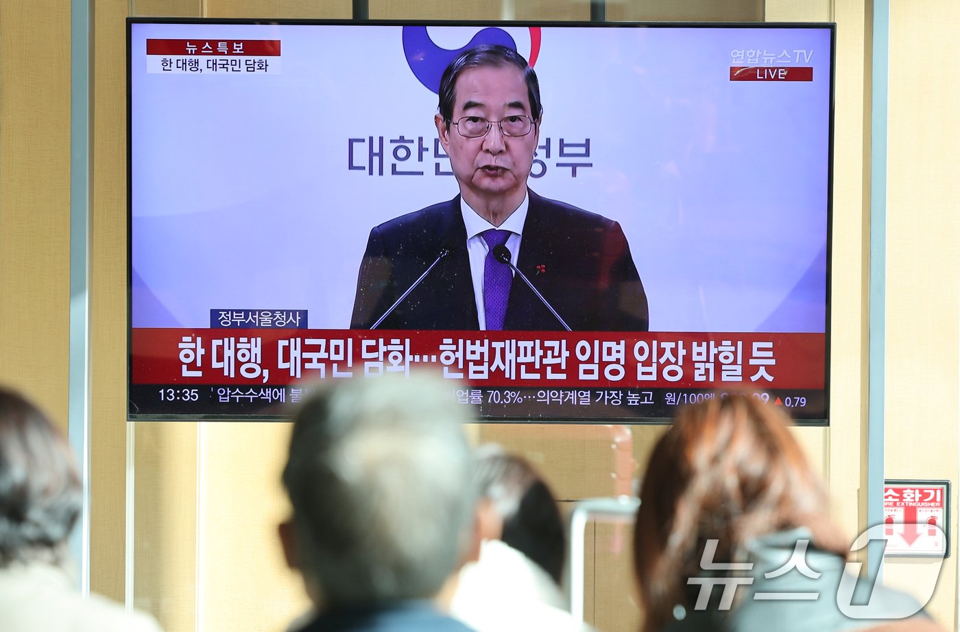 본문 이미지 - 시민들이 26일 서울역 대합실에서 한덕수 대통령 권한대행 국무총리의 대국민 담화를 시청하고 있다. 한 권한대행 이날 대국민 담화에서 "여야가 합의해 안을 제출하실 때까지 저는 헌법재판관 임명을 보류하겠다＂고 밝혔다. 2024.12.26/뉴스1 ⓒ News1 신웅수 기자