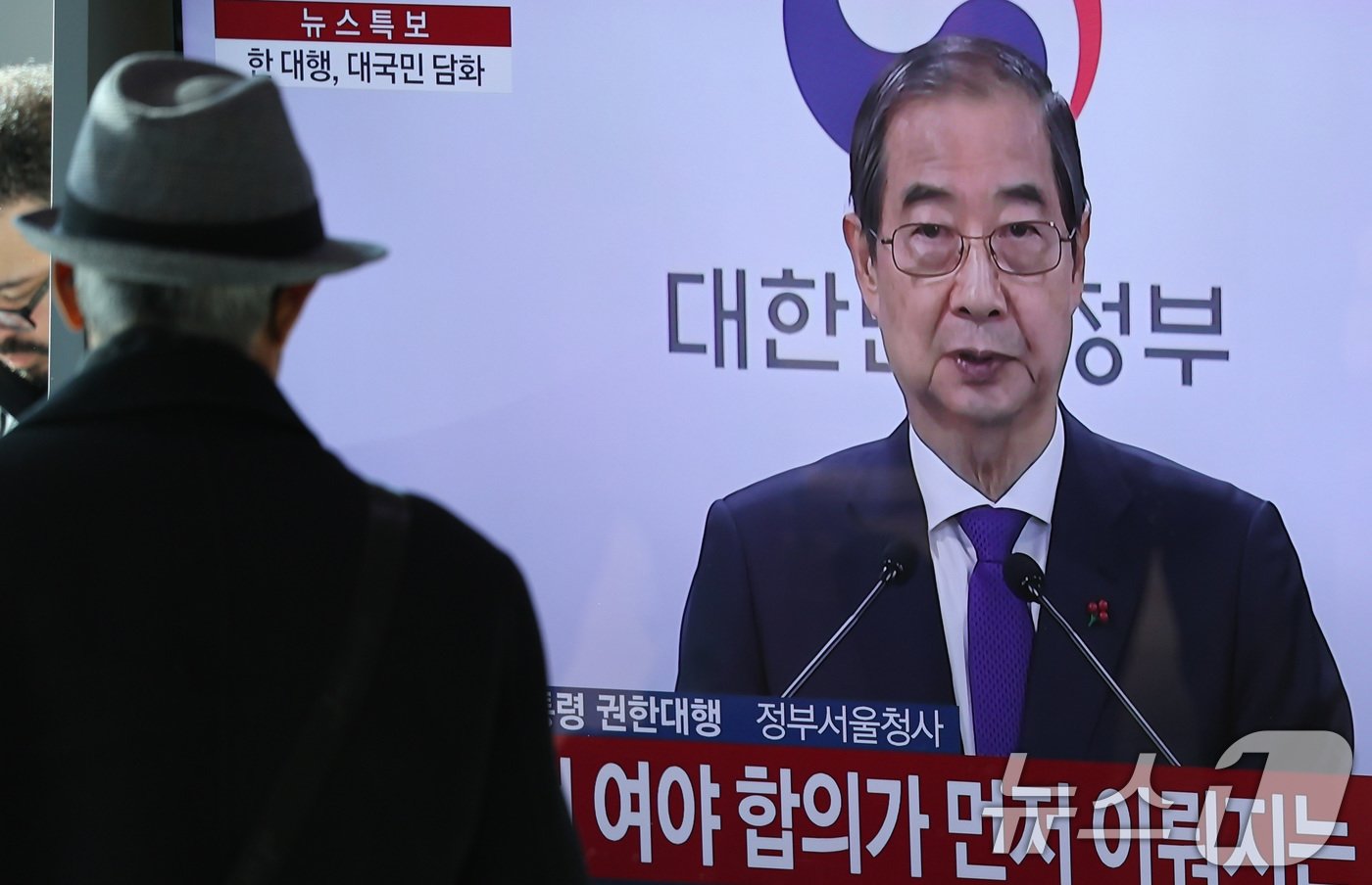 본문 이미지 - 시민들이 26일 서울역 대합실에서 한덕수 대통령 권한대행 국무총리의 대국민 담화를 시청하고 있다. 한 권한대행 이날 대국민 담화에서 "여야가 합의해 안을 제출하실 때까지 저는 헌법재판관 임명을 보류하겠다＂고 밝혔다. 2024.12.26/뉴스1 ⓒ News1 신웅수 기자