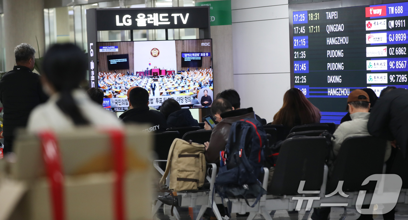 (제주=뉴스1) 오현지 기자 = 7일 오후 제주국제공항 대합실에서 관광객들이 윤석열 대통령 탄핵소추안 표결과 김건희 특검법 재의결 국회 본회의 TV 생중계를 시청하고 있다. 202 …