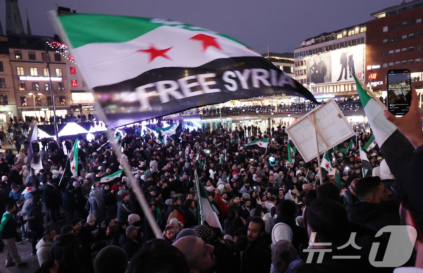 본문 이미지 - 시리아 반군이 수도 다마스쿠스를 점령하면서 사실상 13년간 이어진 내전에 종지부를 찍은 가운데 8일&#40;현지시간&#41; 스웨덴 스톡홀름시티역 광장에 모인 시리아인들이 아사드 정권 붕괴에 환호하고 있다. 2024.12.9/뉴스1 ⓒ News1 박지혜 기자