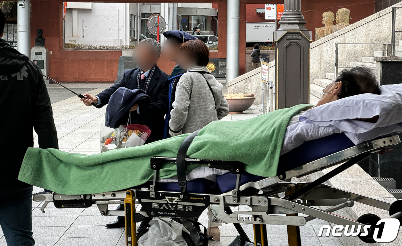 (서울=뉴스1) 유승관 기자 = 26일 서울시내 한 의과대학 졸업식에서 기념 촬영을 하는 한 졸업생 가족 앞으로 환자가 이송되고 있다.교육부에 따르면 정부의 의대 정원 확대 방침에 …