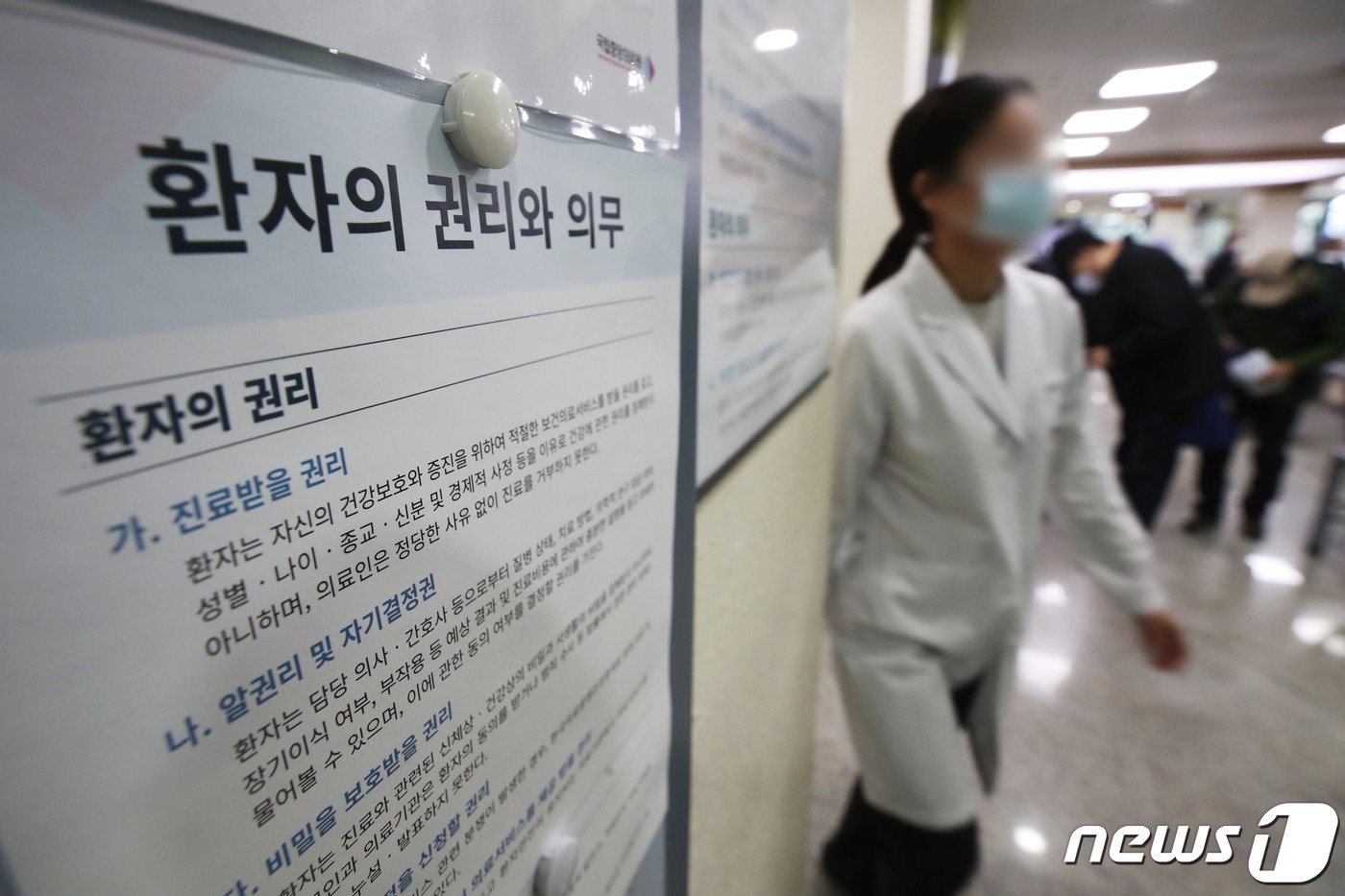 본문 이미지 - 의대정원 증원에 반대하는 전공의들의 집단 행동이 이어지고 있는 13일 서울시내 병원에서 한 의료진이 '환자의 권리와 의무' 게시물 앞을 지나고 있다. 이날 한덕수 국무총리는 의사 집단행동 중앙재난안전대책본부 회의에서 의과대학 정원 증원 재논의 등을 요구하는 의대 교수들에게 "명분 없는 집단행동에 동참하는 대신, 제자들이 환자 곁으로 돌아오도록 적극 설득해달라＂고 밝혔다. 2024.3.13/뉴스1 ⓒ News1 이광호 기자