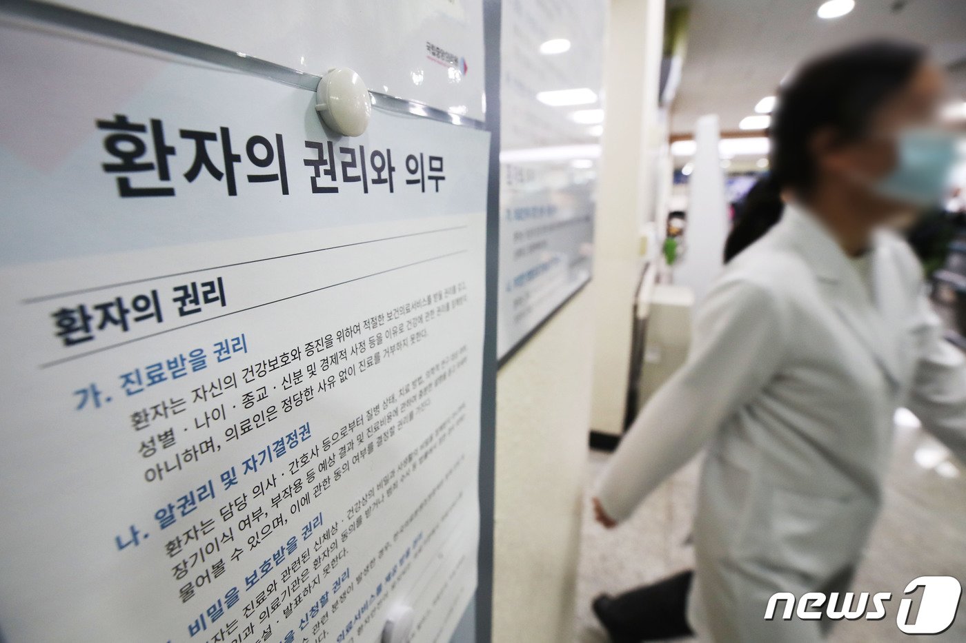 본문 이미지 - 의대정원 증원에 반대하는 전공의들의 집단 행동이 이어지고 있는 13일 서울시내 병원에서 한 의료진이 '환자의 권리와 의무' 게시물 앞을 지나고 있다. 이날 한덕수 국무총리는 의사 집단행동 중앙재난안전대책본부 회의에서 의과대학 정원 증원 재논의 등을 요구하는 의대 교수들에게 "명분 없는 집단행동에 동참하는 대신, 제자들이 환자 곁으로 돌아오도록 적극 설득해달라＂고 밝혔다. 2024.3.13/뉴스1 ⓒ News1 이광호 기자