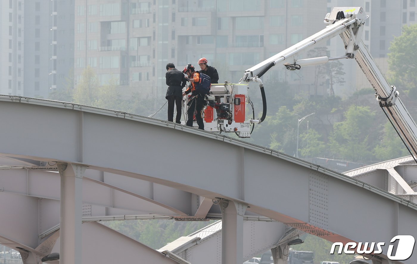 본문 이미지 - 17일 오전 서울 한강대교 노량진 방면에서 교량 위에 올라가 소동을 벌이고 있는 신원을 알 수 없는 남성이 현장에 출동한 소방대원의 설득 끝에 내려올 준비를 하고 있다. 2024.4.17/뉴스1 ⓒ News1 김도우 기자