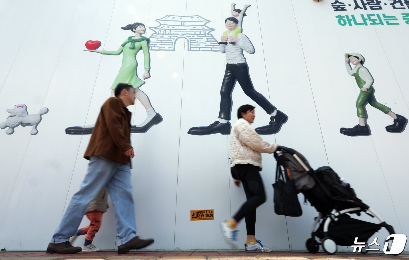 서울 도심의 공사장 가림막에 그려진 행복한 가족 그림 앞으로 유모차를 미는 외국인 가족이 지나고 있다. 2024.4.24/뉴스1 ⓒ News1 박정호 기자