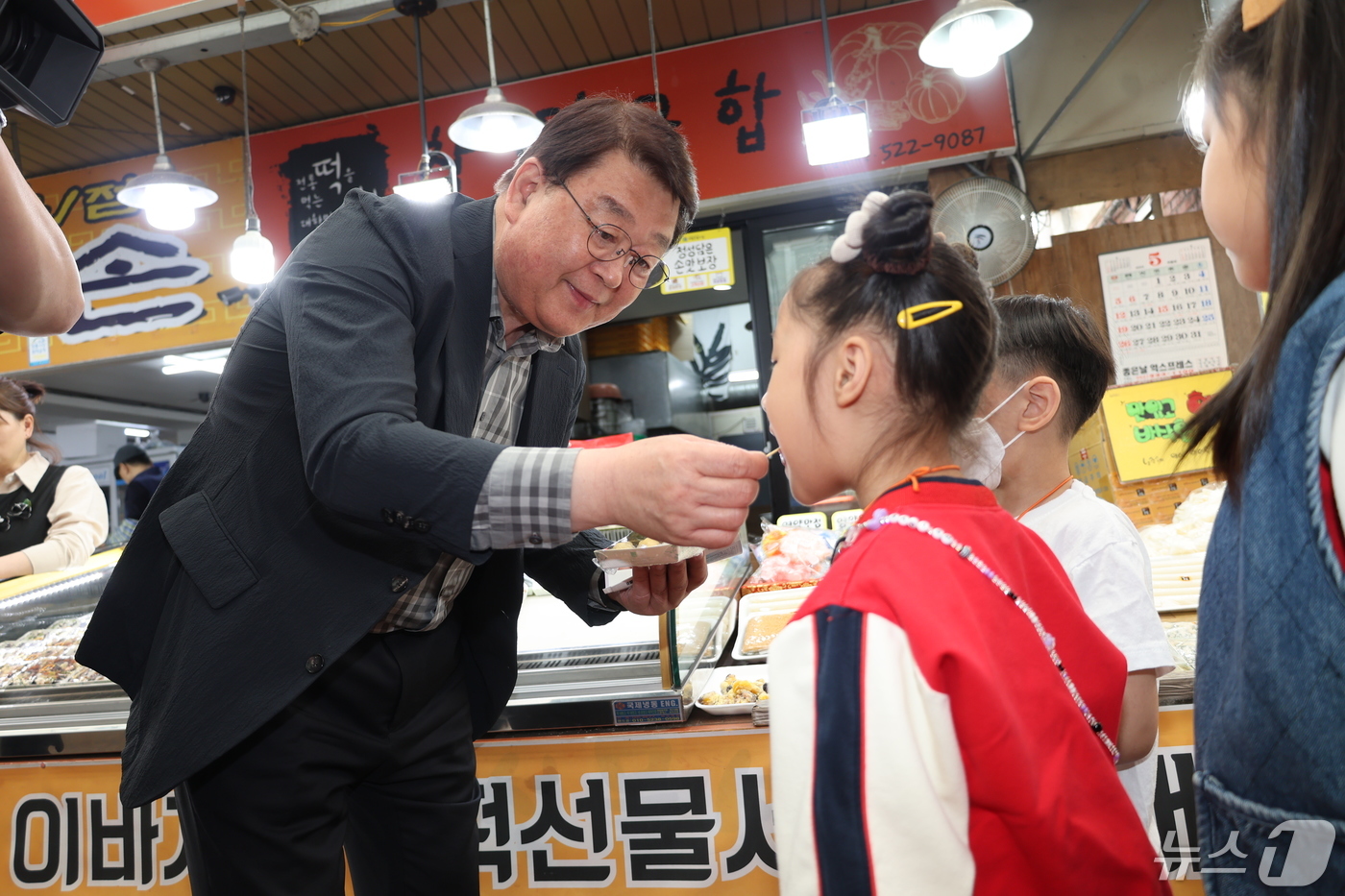 (서울=뉴스1) = 박성효 소상공인시장진흥공단 이사장이 14일 오전 대전 중구 태평시장에서 열린 '어린이 전통시장 체험행사'에서 어린이에게 떡을 먹여주고 있다. (소상공인시장진흥공 …