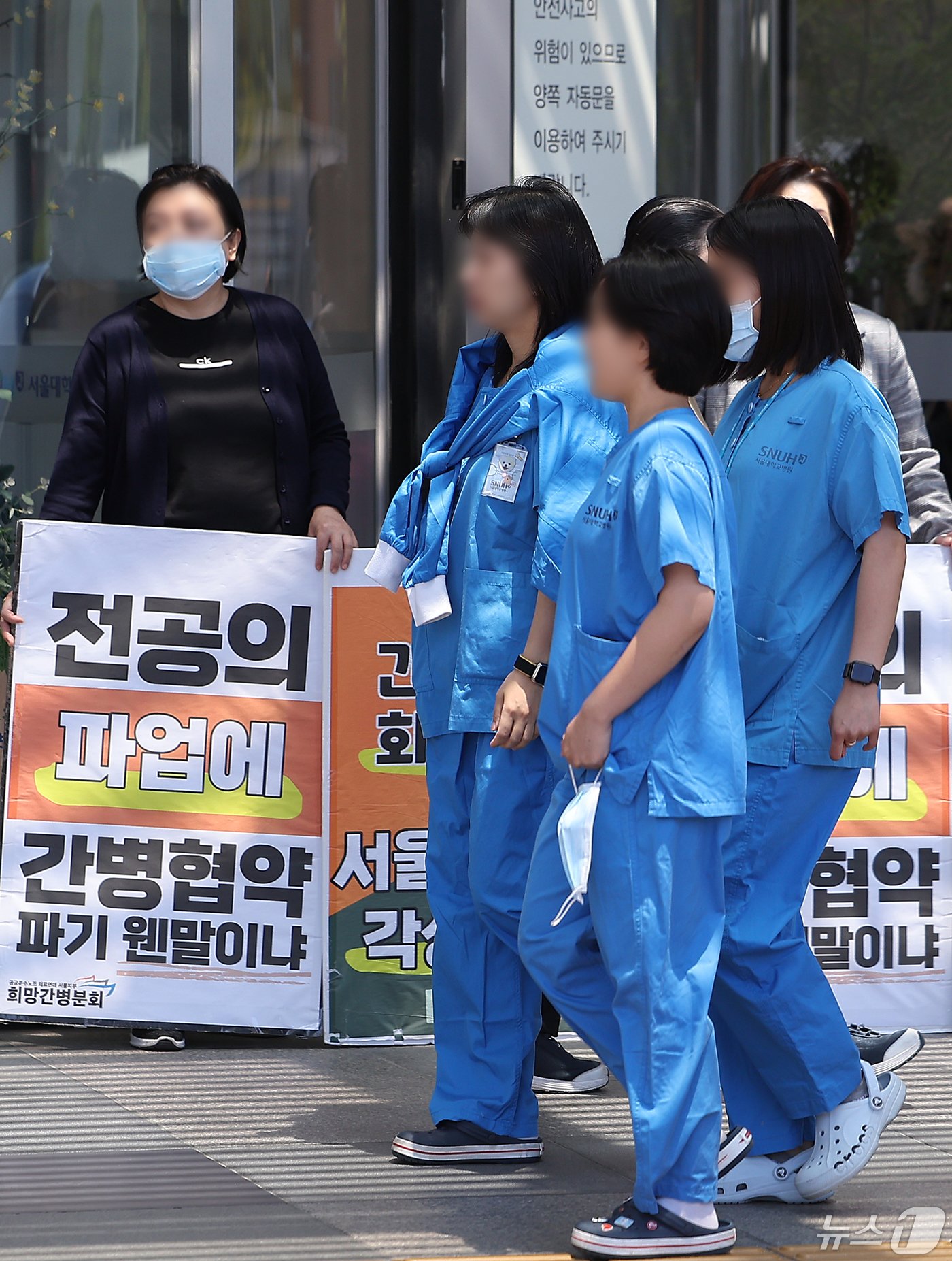 본문 이미지 - 정부의 2025학년도 의대 증원 추진에 대한 법원 판단을 앞두고 있는 16일 오후 서울 시내의 대형병원에서 의료진들이 공공운수노조 희망간병분회의 간병협약 파기 반대 피켓 앞으로 지나고 있다. 2024.5.15/뉴스1 ⓒ News1 김진환 기자