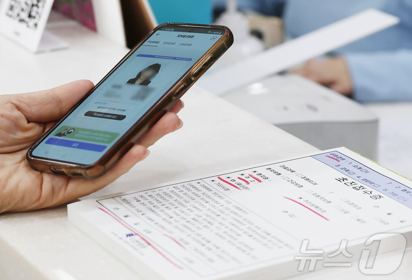 본문 이미지 - 건강보험 본인확인 의무화 제도가 시행된 20일 오전 서울 동작구 한 병원에서 시민이 접수를 하며 모바일신분증을 보여주고 있다.  2024.5.20/뉴스1 ⓒ News1 김민지 기자