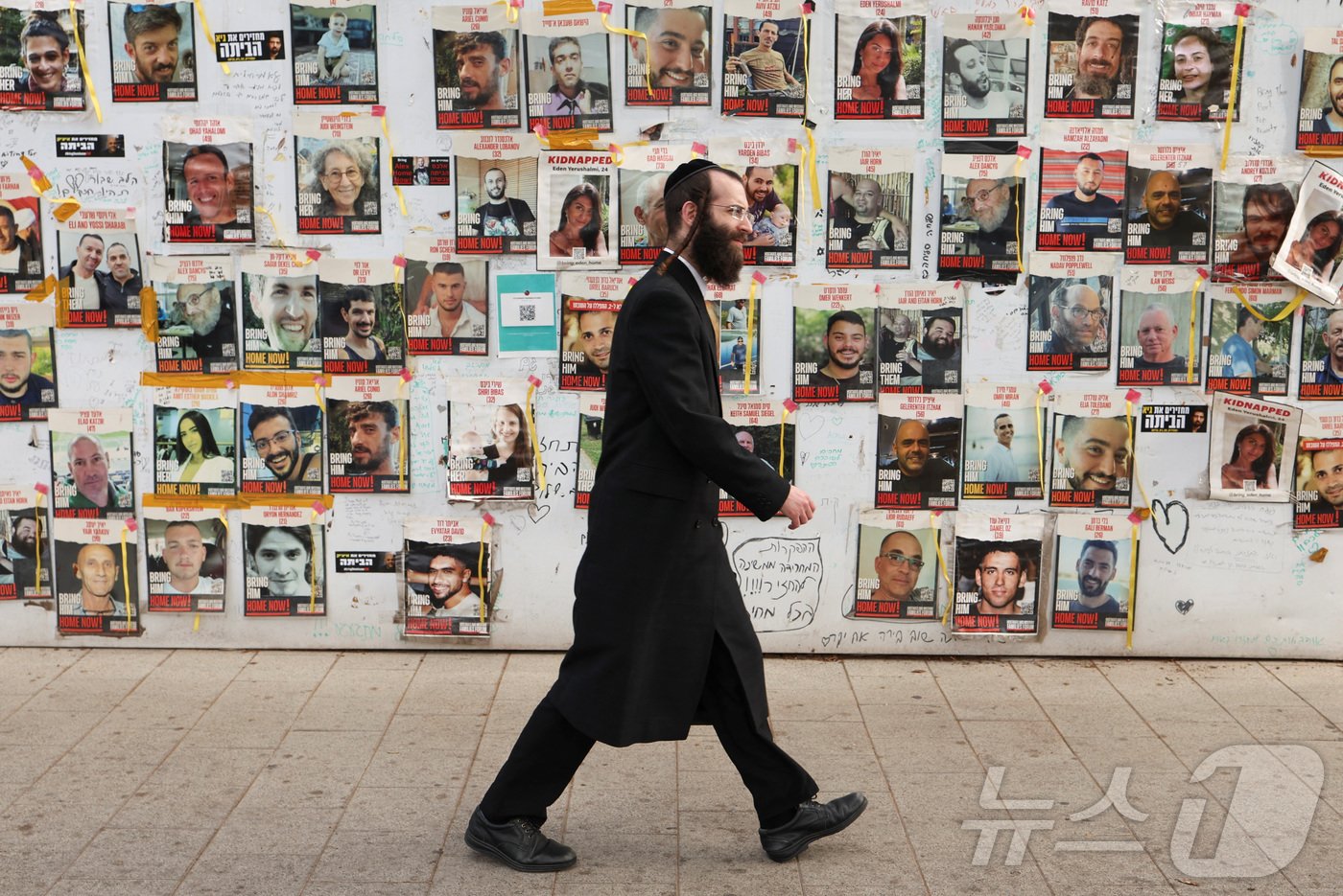 본문 이미지 - 이스라엘 텔아비브의 디젠코프 광장에서 초정토파 유대인 남성이 지난해 10월7일 하마스에 의해 납치된 인질들의 석방을 기원하는 포스터 앞을 지나고 있다. 2024.05.21. ⓒ 로이터=뉴스1 ⓒ News1 정윤영 기자