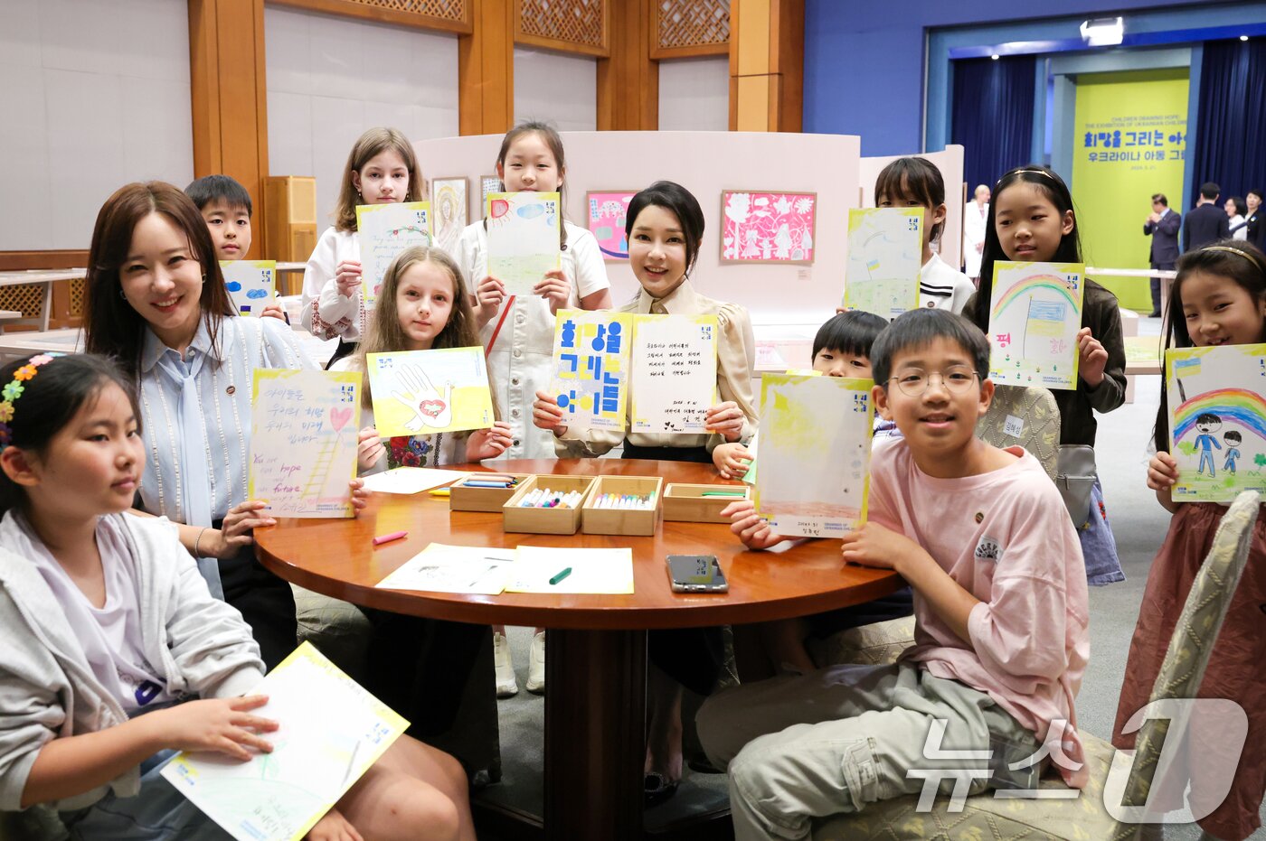 본문 이미지 - 윤석열 대통령 부인 김건희 여사가 21일 청와대 춘추관에서 열린 '희망을 그리는 아이들: 우크라이나 아동 그림전'을 찾아 아이들과 함께 희망의 메시지를 들고 기념촬영을 하고 있다. (대통령실 제공) 2024.5.21/뉴스1 ⓒ News1 오대일 기자