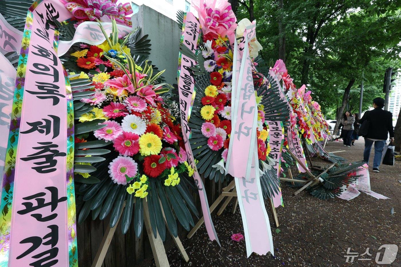 본문 이미지 - 7일 서울 서초구 서초중앙로 서울중앙지방법원과 서울고등법원 등이 위치한 서울법원종합청사 외부 인도에 서울고법 행정7부 재판부를 응원하는 화환이 놓여 지나는 시민들의 눈길을 끌고 있다. 의대교수·전공의·의대생·수험생 등이 신청한 의과대학 정원 증원 집행정지를 심리하고 있는 서울고법 행정7부&#40;부장판사 구회근&#41;는 정부 측에 &#39;증원 규모를 2000명으로 정한 과학적 근거&#39;를 내라고 요구했으며, 또 집행정지 항고심 결정 전까지 정원 최종 승인을 하지 말라고 권고했다. 2024.5.7/뉴스1 ⓒ News1 박정호 기자