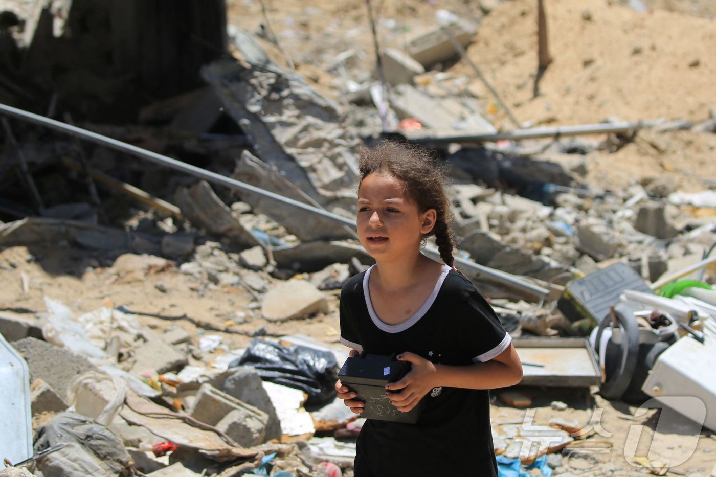 (칸유니스 AFP=뉴스1) 정지윤기자 = 한 팔레스타인 소녀가 11일 이스라엘군 공습에 무너져 내린 가자 남부 칸유니스시 건물 잔해들 사이에서 물건을 찾아 들고 나오고 있다 202 …
