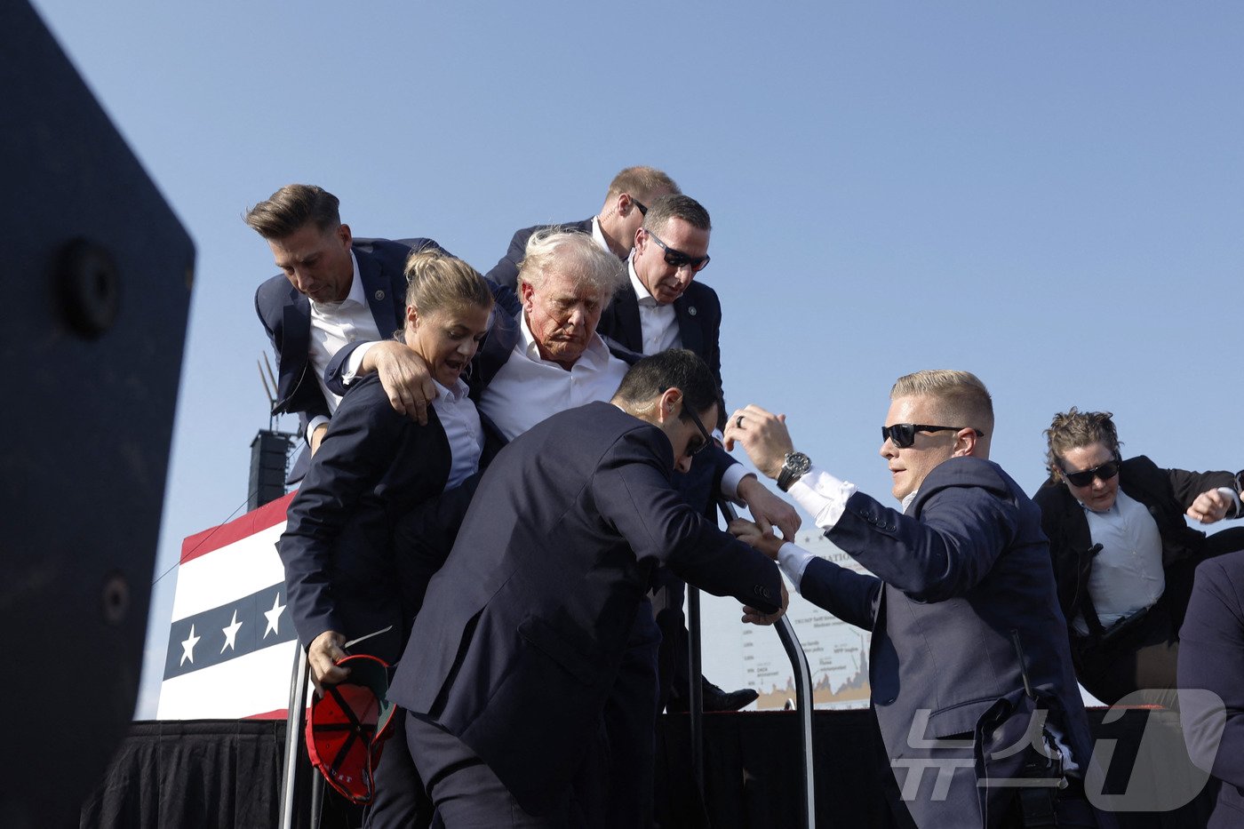 본문 이미지 - 도널드 트럼프 전 미국 대통령이 13일 (현지시간) 펜실베이니아주 버틀러에서 열린 선거 집회서 유세를 하던 중 총격 사건이 발생해 얼굴에 핏자국을 묻은 가운데 경호원들이 긴급하게 대피를 시키고 있다. 2024.07.14 ⓒ AFP=뉴스1 ⓒ News1 우동명 기자