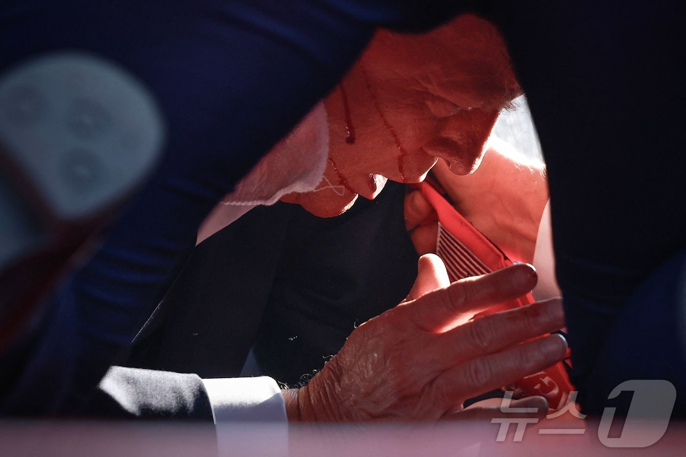 본문 이미지 - 도널드 트럼프 전 미국 대통령이 13일 (현지시간) 펜실베이니아주 버틀러에서 열린 선거 집회서 유세를 하던 중 총격 사건이 발생해 얼굴에 핏자국을 묻은 가운데 경호원들의 보호를 받고 있다. 2024.07.14 ⓒ AFP=뉴스1 ⓒ News1 우동명 기자