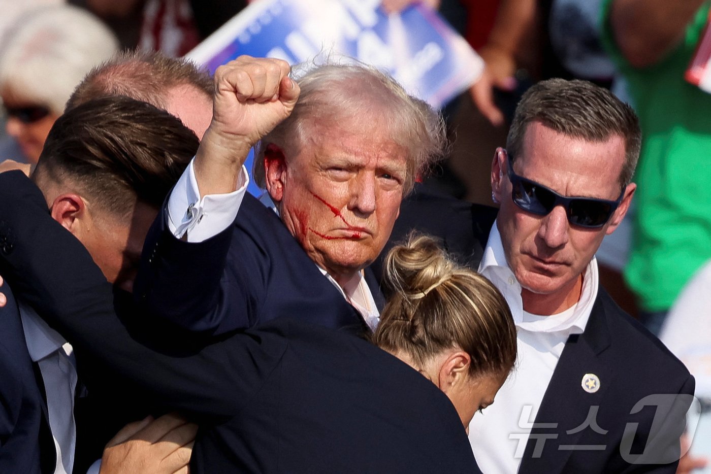 본문 이미지 - 지난 7월 13일(현지시간) 도널드 트럼프 미국 전 대통령이 미국 펜실베이니아주 버틀러의 유세 현장에서 총격에 맞은 후 경호원들의 부축을 받는 사이 지지자들에게 주먹을 들어보이고 있다. 2024.07.13 ⓒ 로이터=뉴스1 ⓒ News1 정지윤 기자